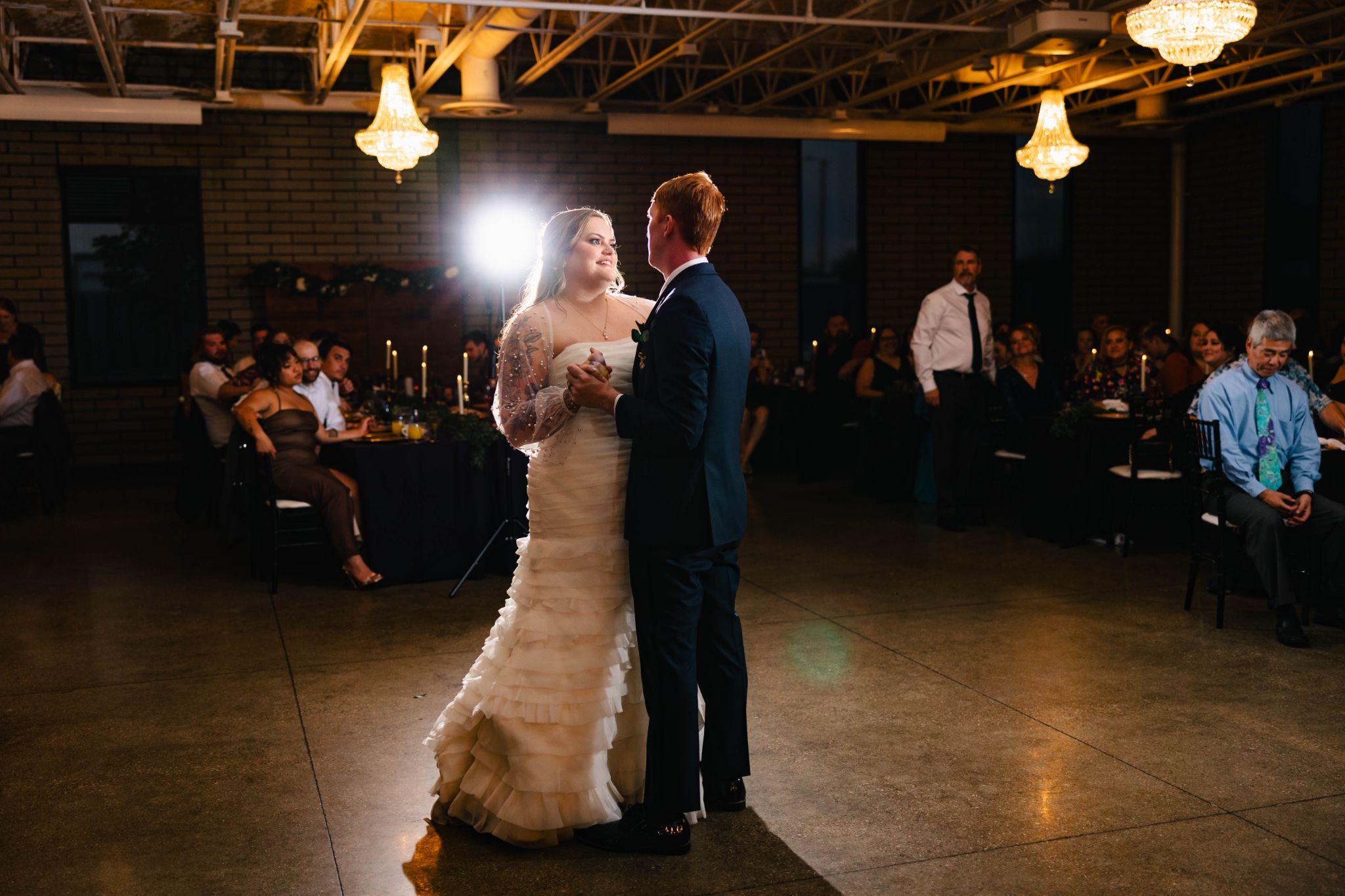 Newlyweds share their first dance at wedding reception, surrounded by love and joy.